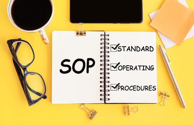 SOP Standard Operating Procedure-tekst op notitieblok en kantooraccessoires op geel bureau