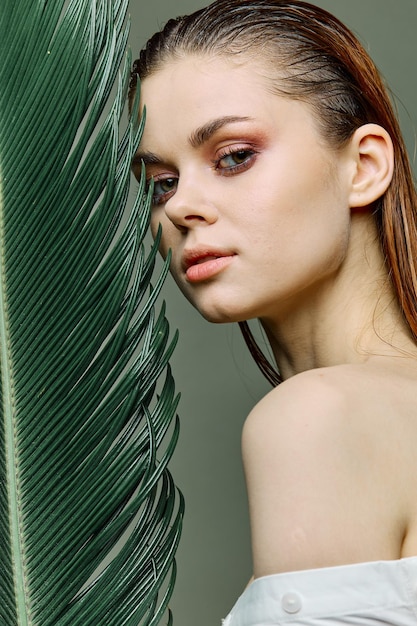 A sophisticated elegant woman with evening makeup stands with a green palm leaf covering part of her face with it Close vertical portrait photo without retouching