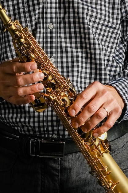 Soprano saxophone in hands on a black background