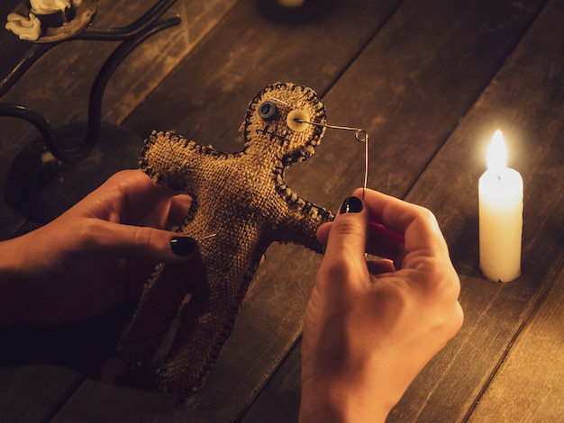 A sorceress pierces a voodoo doll with a pin, causing harm or damage to a person, closeup.