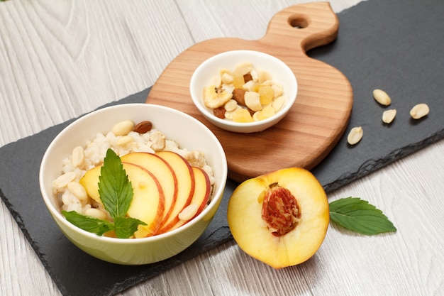 Sorghum porridge with pieces of peach, cashew nuts and almond in porcelain bowls, fresh peach on wooden and stone boards. Vegan gluten-free sorghum salad with fruits.