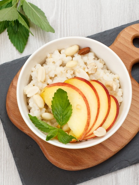 Porridge di sorgo con pezzi di pesca, anacardi e mandorle in ciotole di porcellana su tavole di legno e pietra. insalata di sorgo vegana senza glutine con frutta. vista dall'alto.