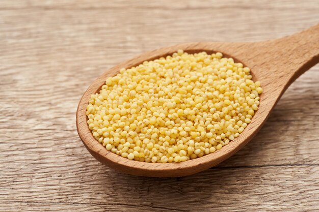 Foto grano di sorgo o di sorgo, grano di miglio o semi di miglio in cucchiaio di legno su fondo di legno della tavola