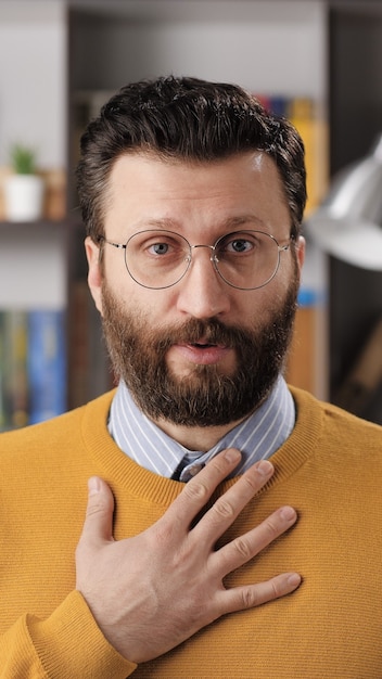 Sorry, man is apologizing and regret. Vertical view of sad bearded male teacher or businessman with glasses looking at camera and sincerely apologizes and says sorry. Medium shot