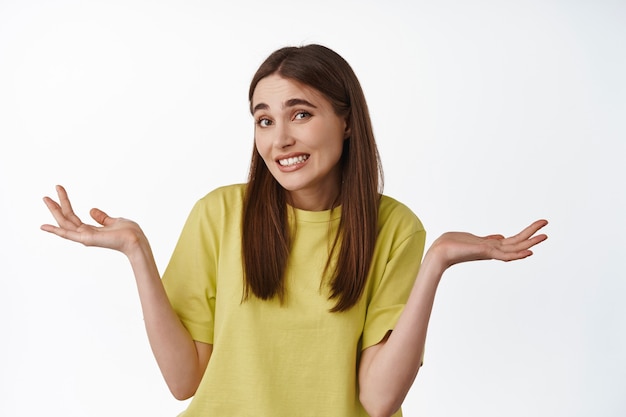 Scusa il mio piccolo, piccolo errore. ragazza imbarazzante che scrolla le spalle e fa un sorriso imbarazzato, non ce la fa, si scusa, sembra all'oscuro, in piedi sul bianco