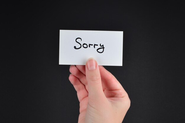 Sorry text on a card in woman  on a black background.