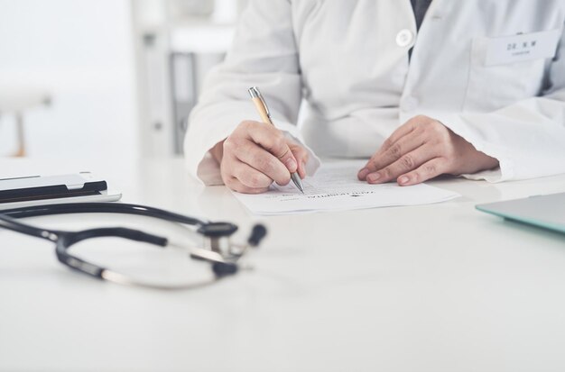 Photo sorting out some patient paperwork cropped shot of an unrecognizable female doctor writing on a document while working in her office