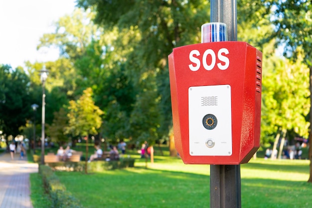 SOS, polizia, pulsante di emergenza nel parco pubblico. Scatola rossa con videocamera e spia blu in alto