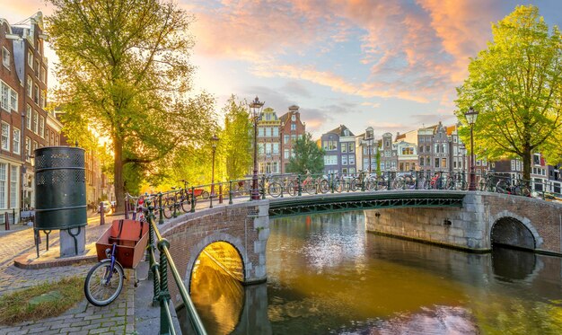 Soul of Amsterdam Early morning in Amsterdam Ancient houses bridges traditional bicycles canals and the sun shines through the trees View of all the sights of Amsterdam