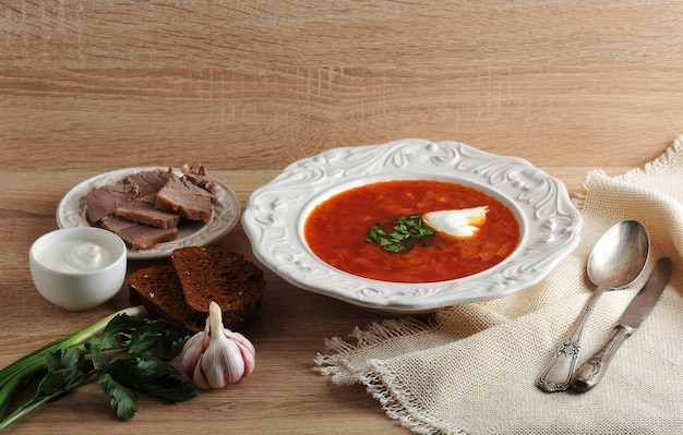 Soup in a bowl with dill, sour cream and black bread on wooden surface