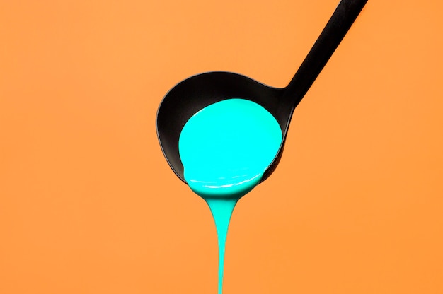 Soup ladle with paint on an orange background