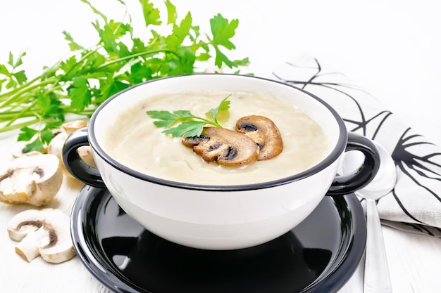 Soup puree from champignons potatoes onions and cream in a bowl napkin parsley and spoon on a background of white wooden board