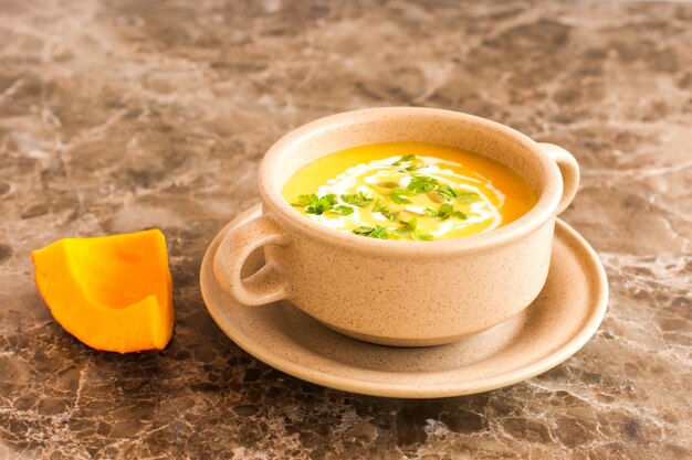 Soup puree of ripe pumpkin in a bowl for soup on a marble background.