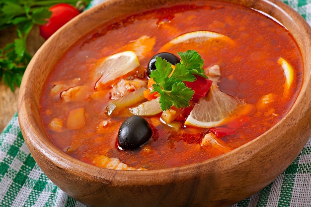 Soup solyanka Russian with meat, olives and gherkins in wooden bowl