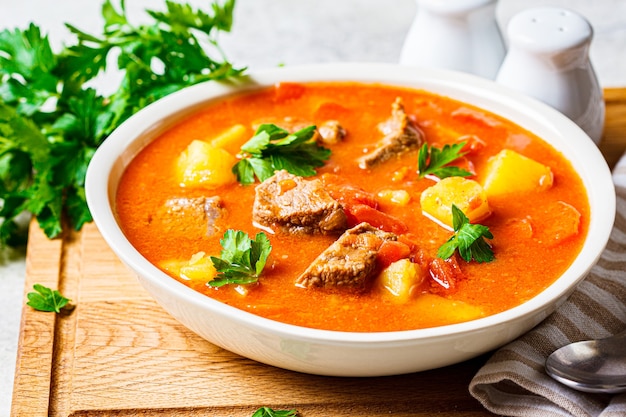 Soup with beef and vegetables in a white plate on a wooden board.