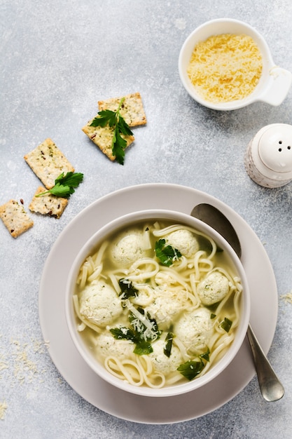 Zuppa con polpette di pollo e pasta d'uovo, parmigiano, prezzemolo in una ciotola di ceramica su un tavolo grigio. brodo tradizionale italiano. vista dall'alto.