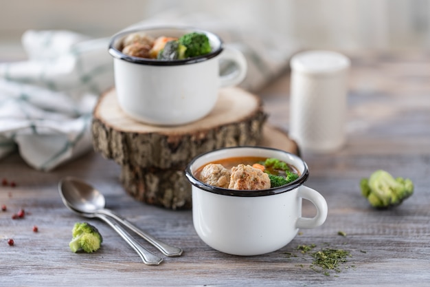 Soup with meatballs in metal mugs on wooden table