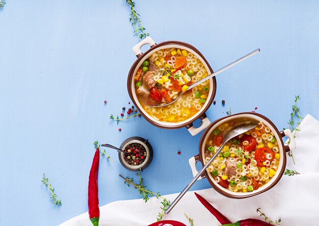 Soup with small pasta, vegetables and pieces of meat in  bowl on  blue table. Italian food. 