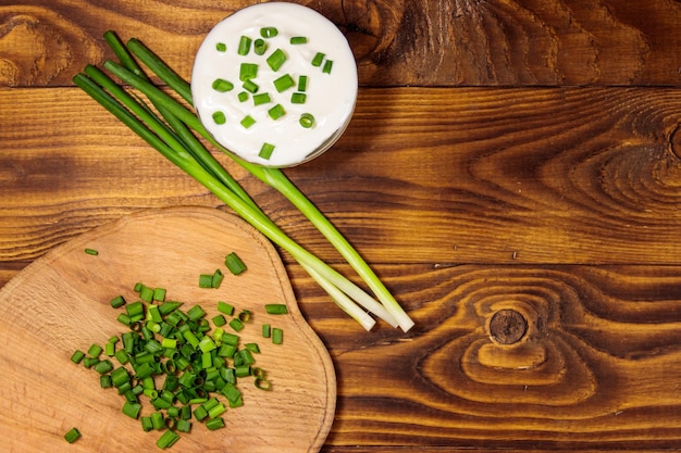 Sour cream and green onion on wooden table. Top view