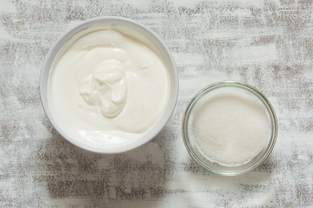 Sour cream in white bowl and sugar in glass bowl on the white background before making cream