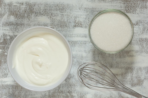 Sour cream in white bowl whisk and sugar in glass bowl on white background before making cream