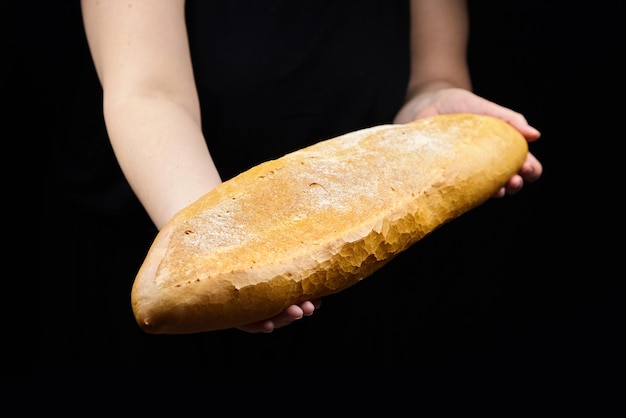Foto prodotto di panetteria a pasta acida su sfondo nero donna tiene pane di grano bianco mano femminile e panino