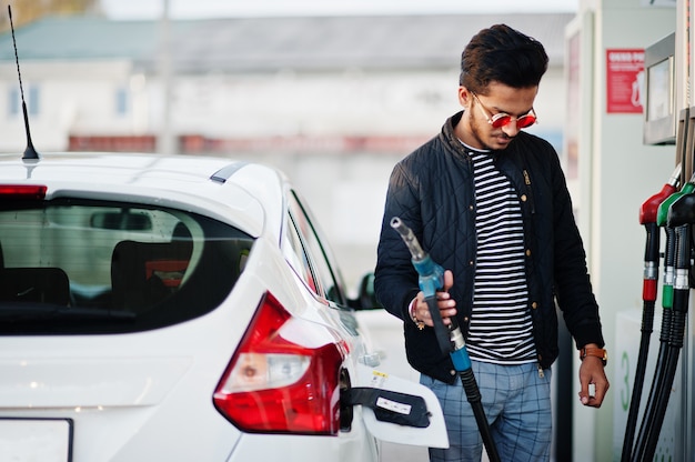 South asian man or indian male refueling his white car on gas station.