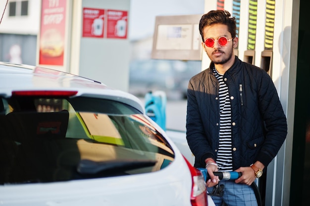 South asian man or indian male refueling his white car on gas station