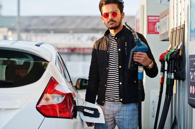 South asian man or indian male refueling his white car on gas station