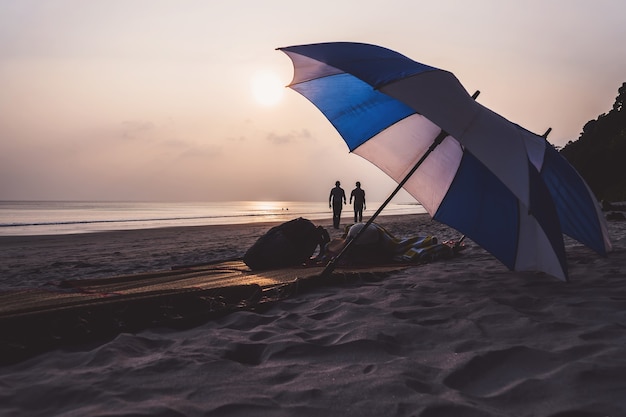 サウスビーチマイアミビーチの傘とラウンジチェア。海に沈む美しい夕日を背景に、人けのない人けのないビーチに横たわる白と青の2つの傘。