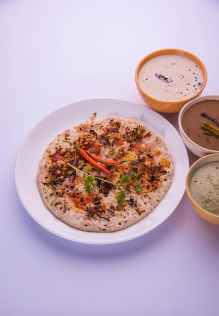 Foto il cibo dell'india meridionale uttapam o ooththappam o uthappa è un piatto simile alla dosa preparato cuocendo gli ingredienti in una pastella, servito con chutney di cocco, chutney verde e sambar