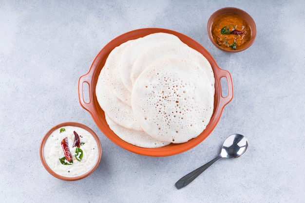 남부 인도 전통 아침 식사 Dosa 또는 Thattu 도사는 흰색 질감의 배경에 반찬 흰색 코코넛 처트니와 양파 처트니가 있는 식기에 배열된 주철 도사 타와를 사용하여 만든 것입니다.