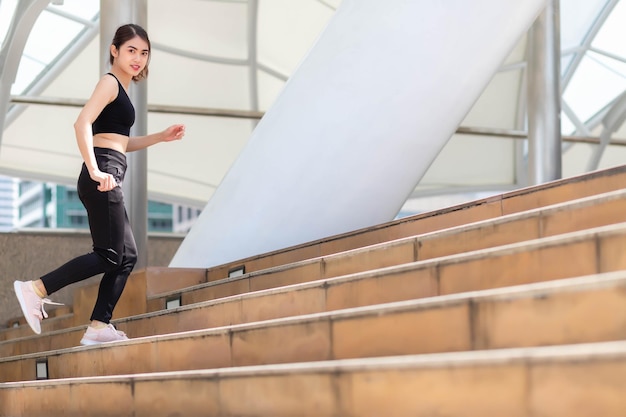 A Southeast Asian woman in gym clothes running up stairs outdoors.