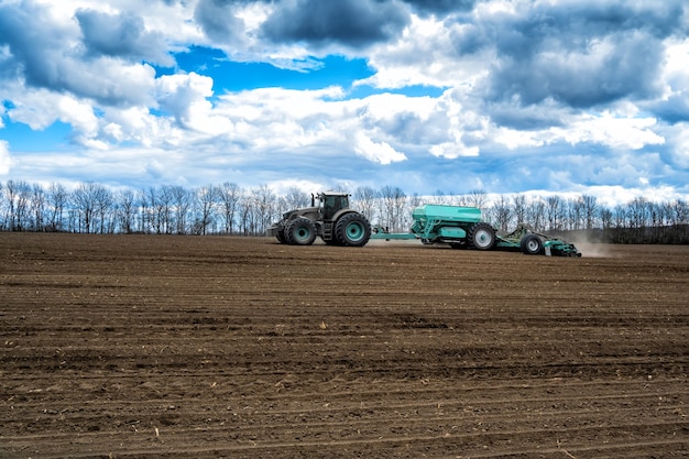 Фото Посевные работы в поле весной. трактор с сеялкой.