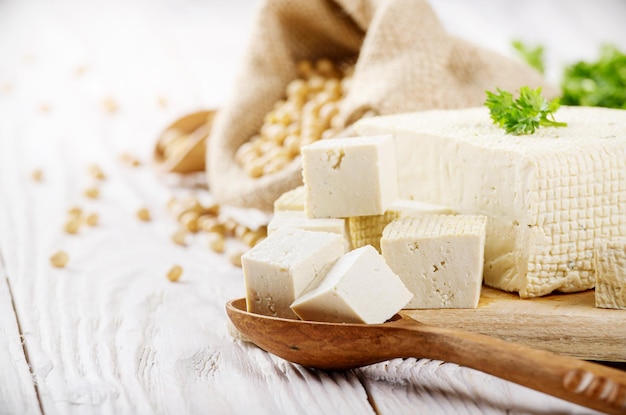 Soy Bean curd tofu on cutting board and in hemp sack on white wooden kitchen table Space for text