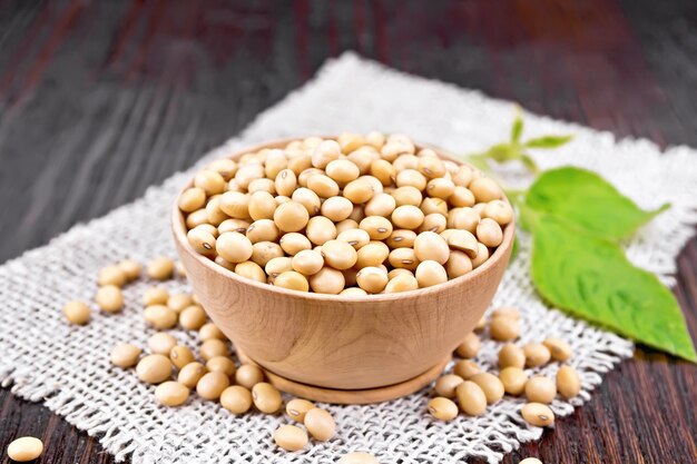 Soy beans in a bowl, green leaf on burlap on wooden board background