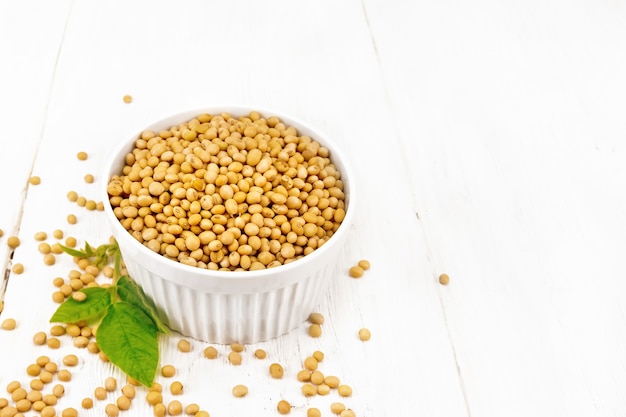 Soy beans in a bowl and on a table, green leaf on wooden board background