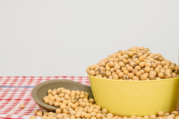 Soy beans fully fill in the bowl on red table against white .