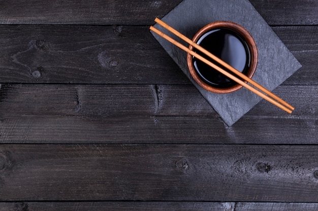 Soy sauce, chopsticks on black stone. Top view