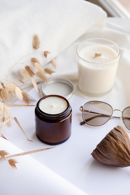 Soy wax aroma candle in brown jar on bed with fashion glasses Candle mockup design