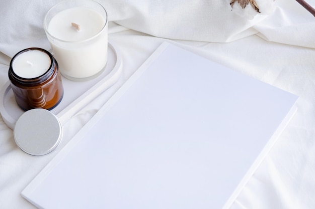 Soy wax aroma candle in white jar on bed with cotton branch Candle and book mockup design