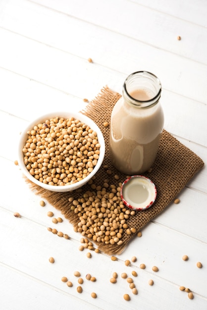 Soya OR Soy milk made by soaking and grinding soybeans, it's a healthy drink served in a bottle with raw whole in a bowl