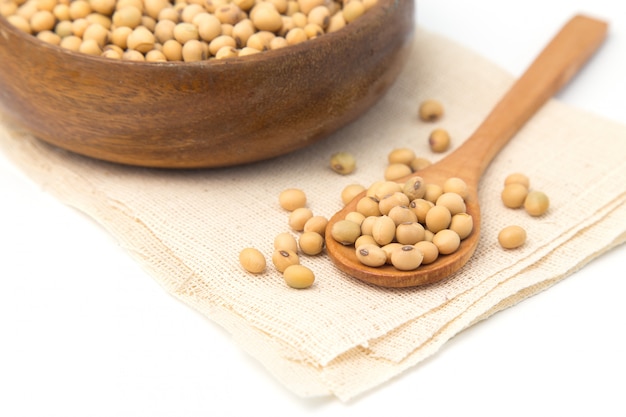 Soybeans in wooden bowl and spoon putting on linen and white background.