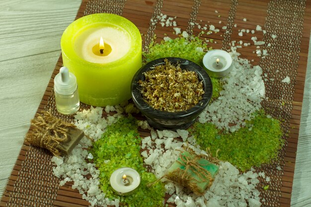 spa accessories with soap, bowl with dried chamomile flowers, bottles with aromatic oil, sea salt, candles on bamboo napkin