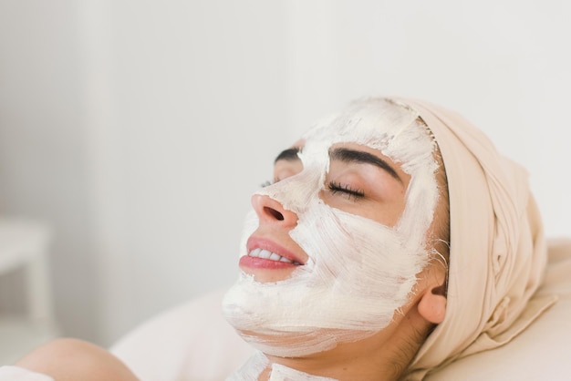 Spa beauty organic facial mask application at day spa salon. Woman applying facial clay mask at spa salon, side view.