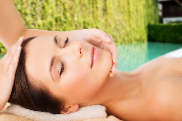 spa, beauty, people and body care concept - beautiful woman getting face treatment over green natural background