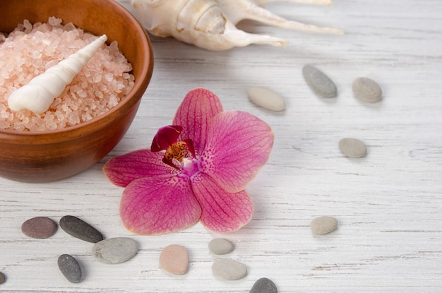 SPA body care concept Bath salts seashells pebbles and pink Orchid flower on white wooden background