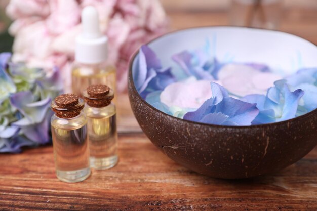 Photo spa composition aromatic water in bowl bottles of essential oil and flowers on wooden table closeup