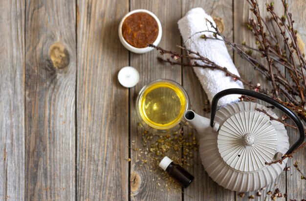 Spa composition in rustic style with a kettle of tea, a natural body care product on a wooden surface.