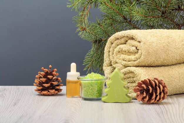 Spa composition with soft terry towel, bottle with aromatic oil, gift box, bowl with sea salt, cones and fir tree branch on gray background